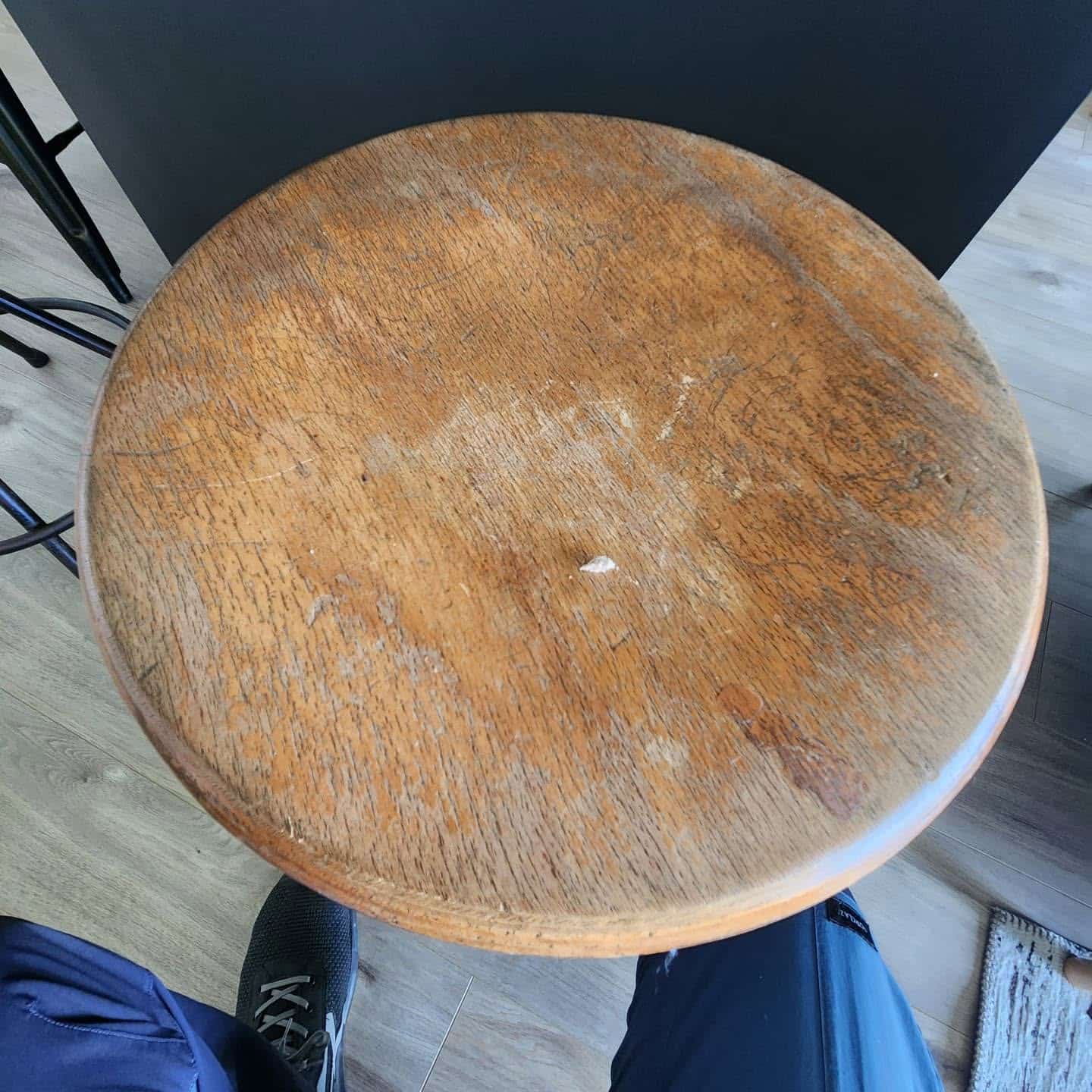 Assise de tabouret ronde en bois massif avec traces d'usure et rayures sur un sol clair.